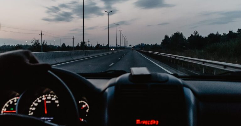 View through a windscreen of a New York highway at dusk, speedometer lit on the dashboard